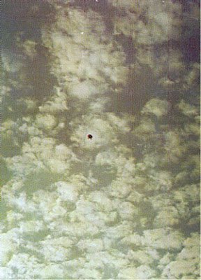 One of the four original 35mm film photographs taken by Manoel Gomes de Moura on the morning of 10 September 1990 at Alfena, showing the dark object suspended against a heavily clouded sky as it pulled away. This is a genuine period photograph, not a model, render, or recreation; the famous leg-like appendages that earned it the "flying jellyfish" nickname are only resolvable on closer enlargements of the negatives.