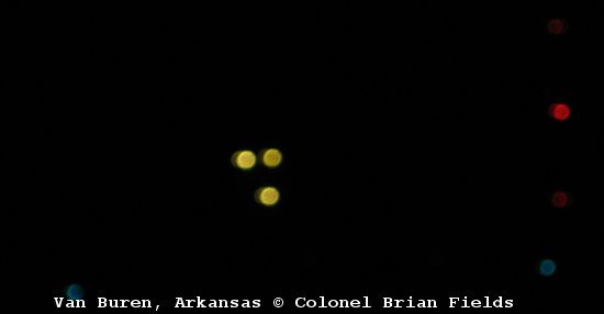 Colonel Brian Fields's own photograph, taken on a 6-megapixel Canon on the evening of 9 January 2007 near Van Buren, Arkansas. Three soft, out-of-focus yellow-orange glows sit in a loose triangle; the vertical string of red and blue lights at the right edge is, per the original WorldNetDaily caption, a local radio tower. The colors and triangular arrangement match LUU-2 parachute illumination flares dropped by A-10s on the nearby Fort Chaffee range that night. This is the genuine witness photograph, not a model, render, or recreation.