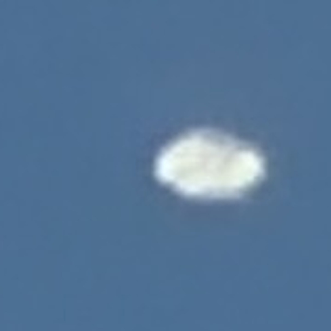The object magnified six times from the original camera file. The outline is lumpy and soft with a faint darker seam across the middle, and there is no hard edge anywhere. The image was taken at a 1049 millimetre equivalent focal length, so this is close to the limit of what the camera recorded.