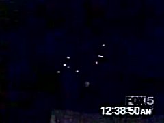 A real video frame grab from contemporary FOX 5 television coverage of the Carteret lights, showing roughly seven to nine bright golden-white lights in a loose V over a dark night sky. The broadcast station bug "FOX 5" and the on-screen timestamp "12:38:50 AM" are visible, matching the reported sighting window of about 12:20 to 12:40 a.m. on 15 July 2001. This is a TV news still, not a sharp photograph, and not a recreation.