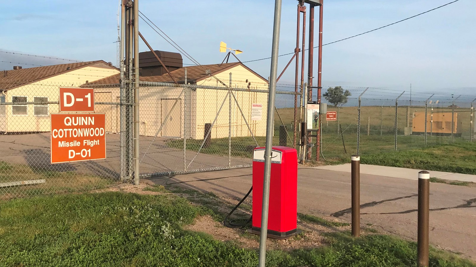 A context photograph, not imagery of the reported event, of which none exists. The gate of the Delta-01 Launch Control Facility in the same Ellsworth Air Force Base missile field, preserved as part of the Minuteman Missile National Historic Site. The sign reads Quinn Cottonwood Missile Flight D-01. Mario Woods was stationed at the November Flight facility, a sister site of the same design, and the perimeter fence and spotlight poles visible here are the fixtures he describes signalling with.