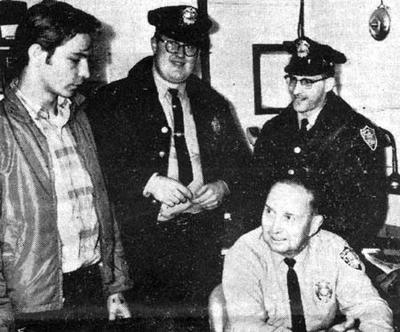 Period press photograph taken at the Exeter, New Hampshire police station in September 1965, showing the three principal witnesses with the desk officer. Left to right: eighteen-year-old Norman Muscarello (in plaid), who first reported the object; Patrolman David Hunt; Patrolman Eugene Bertrand Jr.; and seated, dispatcher Reginald "Scratch" Toland. This is a genuine 1965 newspaper halftone (grayscale), not a recreation or illustration.