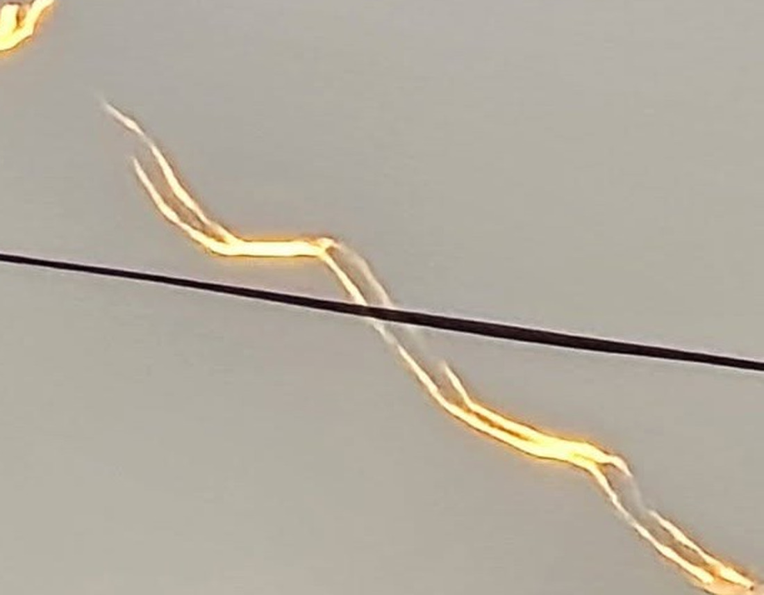 The trail enlarged. Two roughly parallel filaments run alongside each other, the gold lit edge stays on one side of the grey unlit edge throughout, and the regular switchback kinks are the Crow instability growing along the wingtip vortex pair. The detached hook at the top left is a pinched off vortex ring.