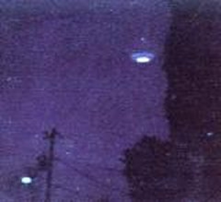 One of Ed Walters' original 1987 Polaroid photographs of the claimed Gulf Breeze craft: a glowing, domed top-shaped object against a dusk sky, with a power line and tree silhouette in the foreground. This is the actual disputed photograph, not a re-creation; an independently recovered foam-plate model was later shown to reproduce this same shape.