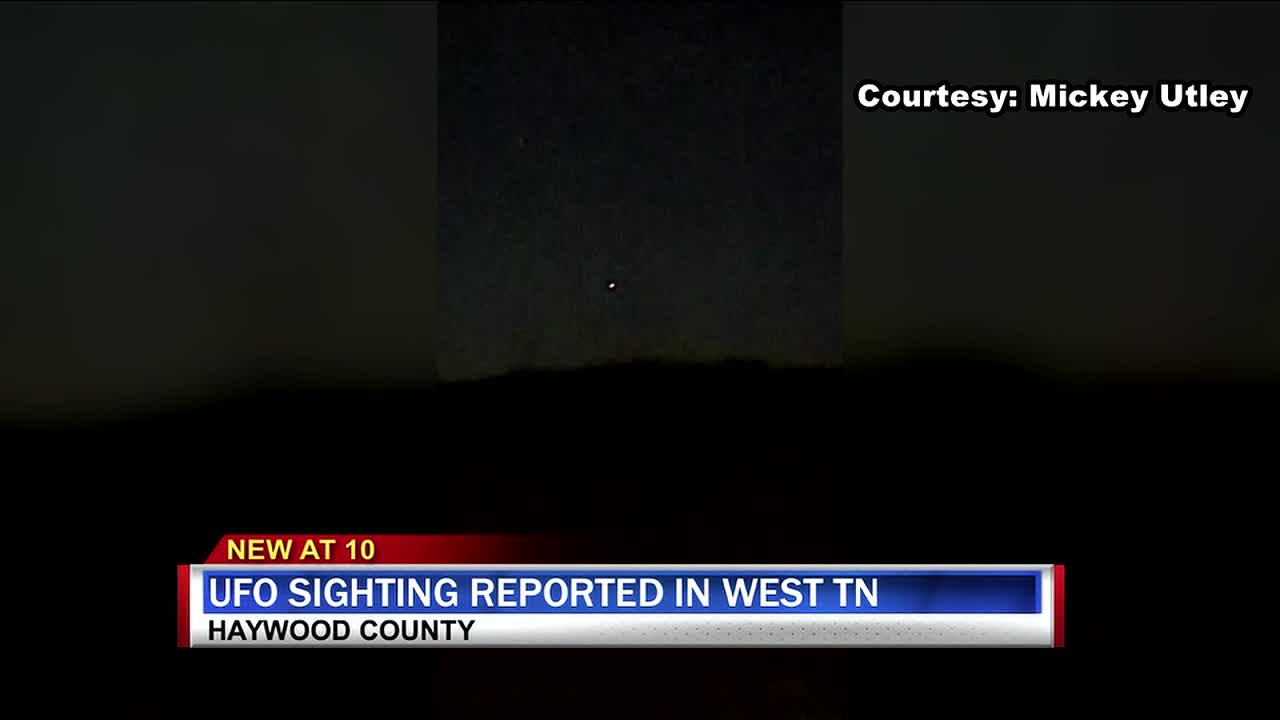 The full broadcast frame at the same moment, brightened. The witness recording is pillarboxed inside the station's 16 by 9 frame, and the object sits above a dark treeline silhouette low in the sky, matching the witness description of a bright light low on the horizon.