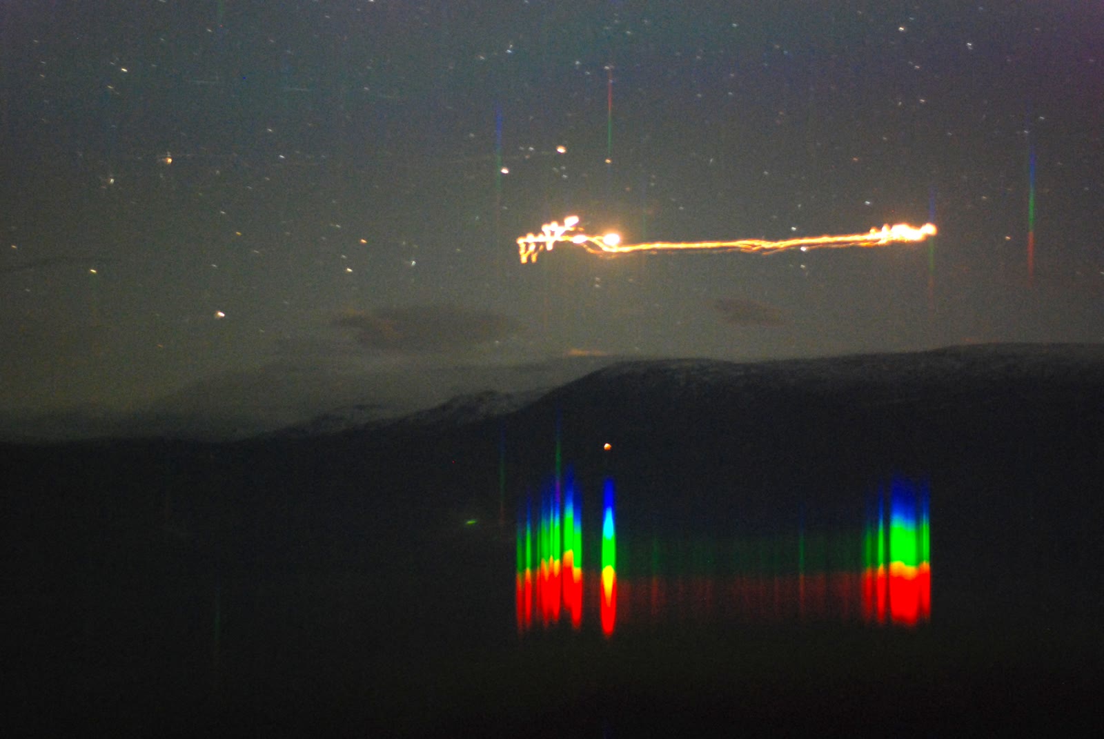 A Hessdalen light over the Finsa ridge on 20 September 2007, photographed through a transmission grating that splits its glow into a continuous spectrum, the coloured bands in the lower frame.