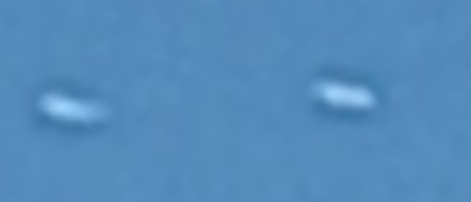 The two objects enlarged eight times from the single photograph in the witness filing. Each is about 40 by 17 pixels in the original, with a bright upper edge and a darker body beneath. The pair sits 166 pixels apart on a line 2.8 degrees off horizontal.