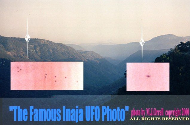 Michael Orrell's own published presentation of the Inaja photograph, captioned by him "The Famous Inaja UFO Photo." This is the real 1 July 1990 landscape frame of the hazy hills above Santa Ysabel, with two pink enlargement insets Orrell added showing the dark specks (nine on the left, one on the right). The white diamond outlines pointing at the two clusters are Orrell's own graphic markers laid over the photo, not objects in the sky. Not a CGI render; the underlying image is the actual photograph, presented with the witness's annotations and copyright line.