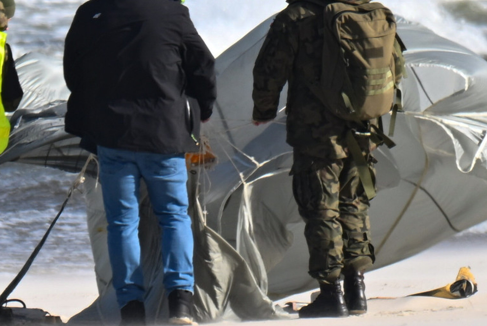 The canopy at roughly two and a half times enlargement. The fabric is panelled, shroud lines are visible running across and away from it, an orange component sits near the centre, and the civilian in frame is holding a bundle of lines. A recovery parachute is standard equipment on the class of training drone the Military Police named, so this part of the photograph supports the official identification rather than merely illustrating it.