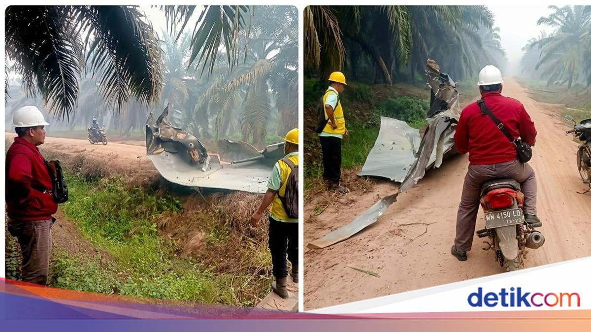 The torn metal sheet where it came to rest beside a plantation road on 19 October 2026, with plantation staff for scale. Haze from the Central Kalimantan fire season is visible among the palms.