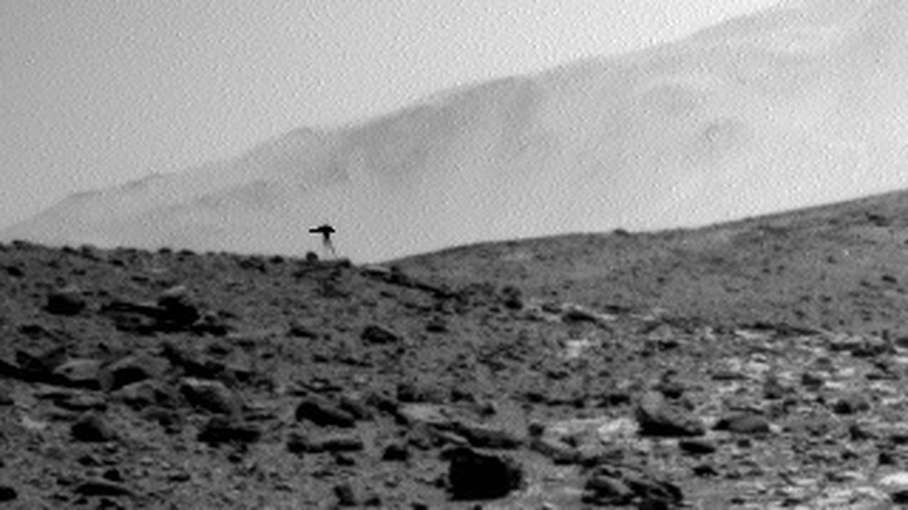 Contrast-enhanced crop of Curiosity right Navcam frame NRB_745839057EDR_S1031528NCAM00594M_, sol 3924, acquired 2023-08-20T22:27:46.827 UTC in Gale Crater. The dark 34 pixel cluster sits on the ridgeline near image coordinate x=133, y=380, silhouetted against bright sky, and reads as a broad horizontal cap above a narrow vertical stalk. It is absent from the two frames taken 13 and 25 seconds earlier at identical mast pointing, NRB_745839044EDR and NRB_745839032EDR. This is the real NASA raw frame with contrast stretched to make the cluster legible, not a reconstruction, model or illustration.