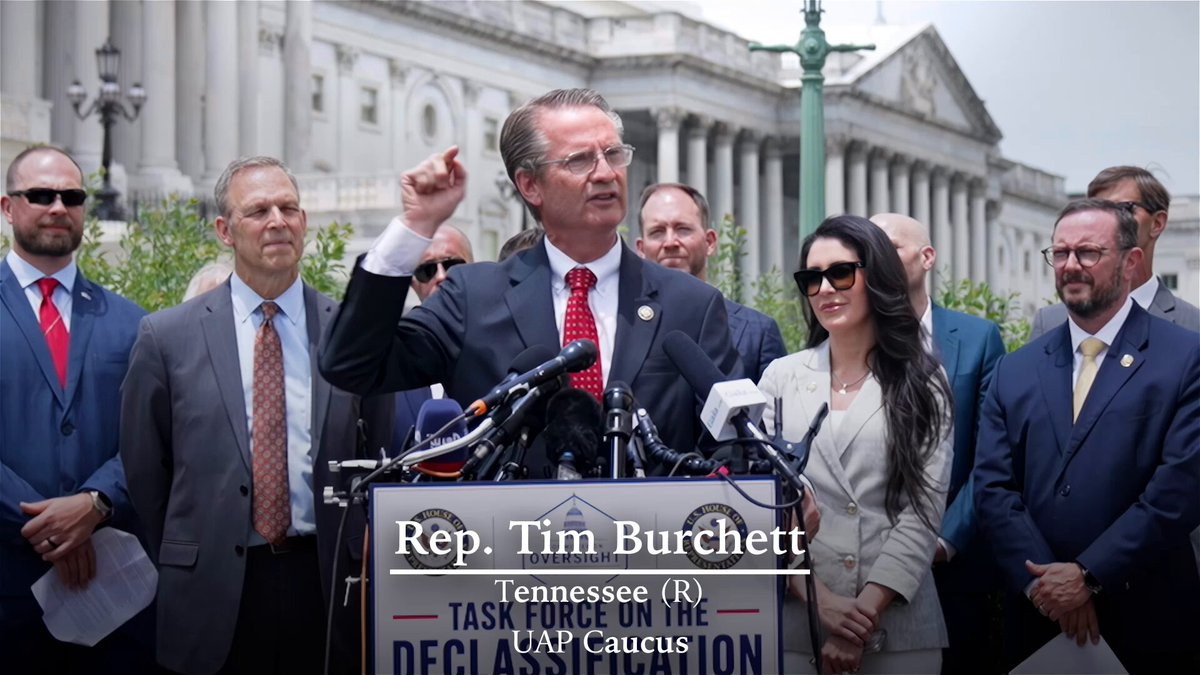 The opening frame of the Mr. President campaign film: Rep. Tim Burchett of Tennessee speaking at a lectern bearing the House Oversight seal and a Task Force on the Declassification of Federal Secrets placard, with Rep. Scott Perry at left and Rep. Anna Paulina Luna at right. This is archival press-conference footage recycled into the film, not new material, and the campaign's own caption identifying Burchett is burned into the picture. No imagery of any craft or occupant appears anywhere in the film or on this page.