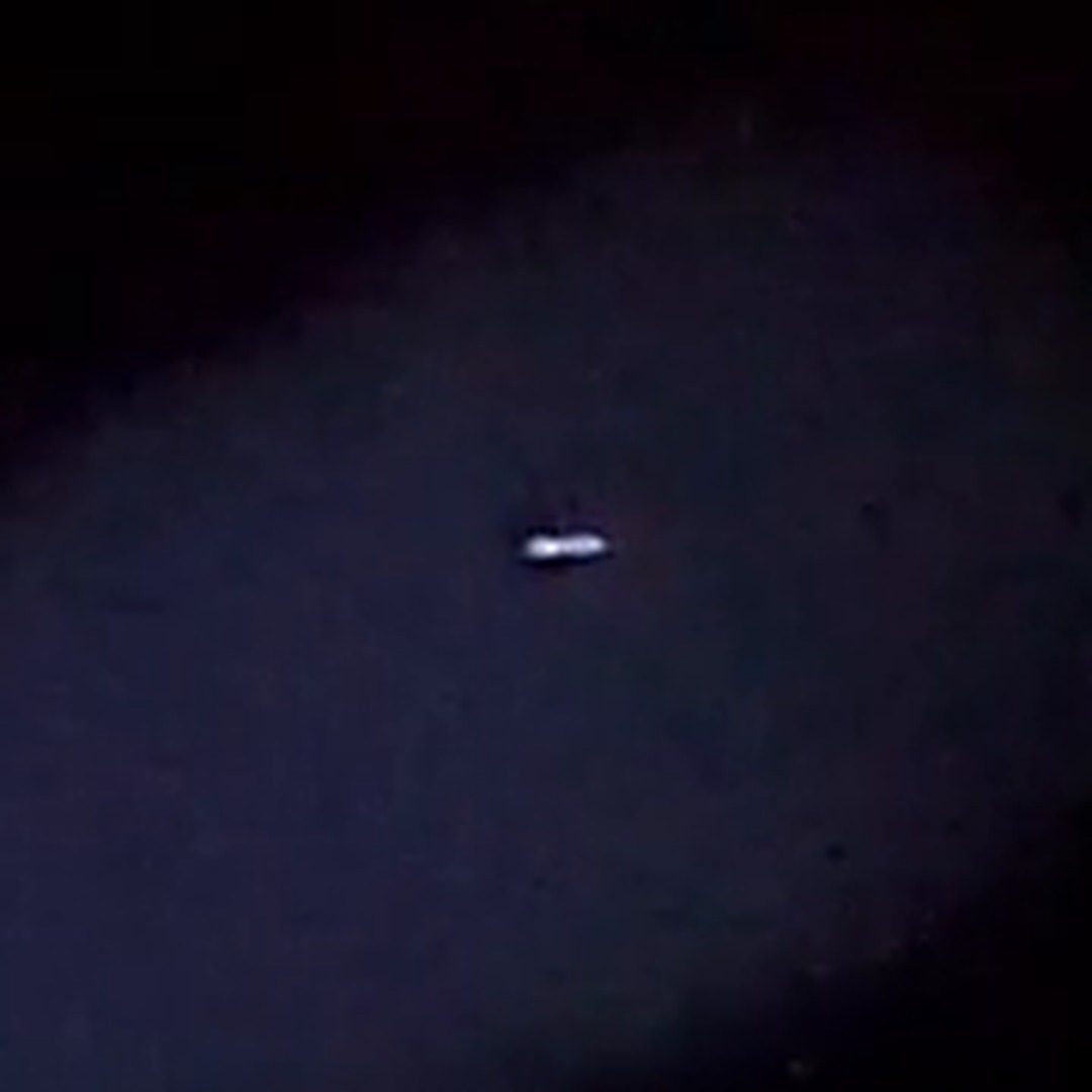 The object magnified six times from the same frame of the first video. It reads as a horizontally elongated bright form with a darker upper edge. The footage resolves no structure beyond this.