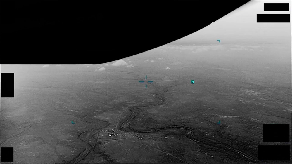 A real frame from the Department of War's own public domain release of DOW-UAP-PR043, taken from the official DVIDS video record. The wide oblique infrared view shows the branching dry channel network of southern Djibouti, with the small compound the analysts used as a terrain reference visible near the lower left. Cyan sensor symbology sits over the picture as a centre crosshair, a north indicator and corner brackets. The rectangular black blocks in the corners are the Department's own redactions of the sensor data overlay, and the manifest flags this record with Redaction set to TRUE. The dark region across the top is sky, which renders dark against warm ground in this infrared polarity. The reported object is not identifiable in this single frame, and the archive is not claiming it is visible here.
