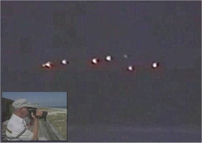 A still from Ralph Fuller's 1988 camcorder video, showing a horizontal row of roughly seven to eight glowing red and orange lights over a darkened Gulf coast beach. The inset photo shows Fuller holding a camcorder to his eye while filming. This is a genuine analog video frame from the tape as later broadcast and circulated, not a recreation or CGI render.