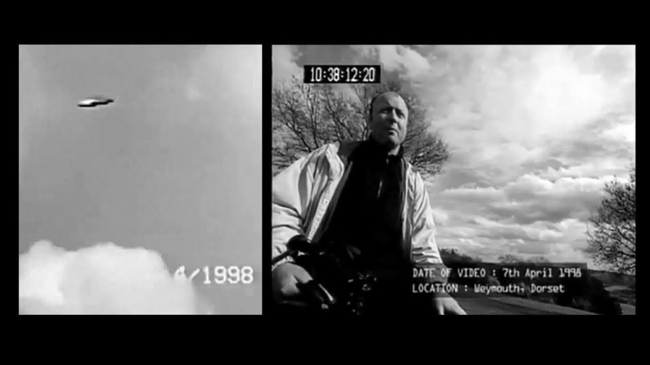 A split-screen still from the actual 7 April 1998 camcorder footage as shown in the documentary "Out of the Blue" (2003): at left, a real video frame of the silver disc-shaped object hovering against cloud near The Ridgeway above Weymouth, Dorset; at right, cameraman Rod Dickinson looking upward, with the documentary's on-screen date and location overlays and the camera timecode visible. This is a genuine video frame, not a render or illustration.