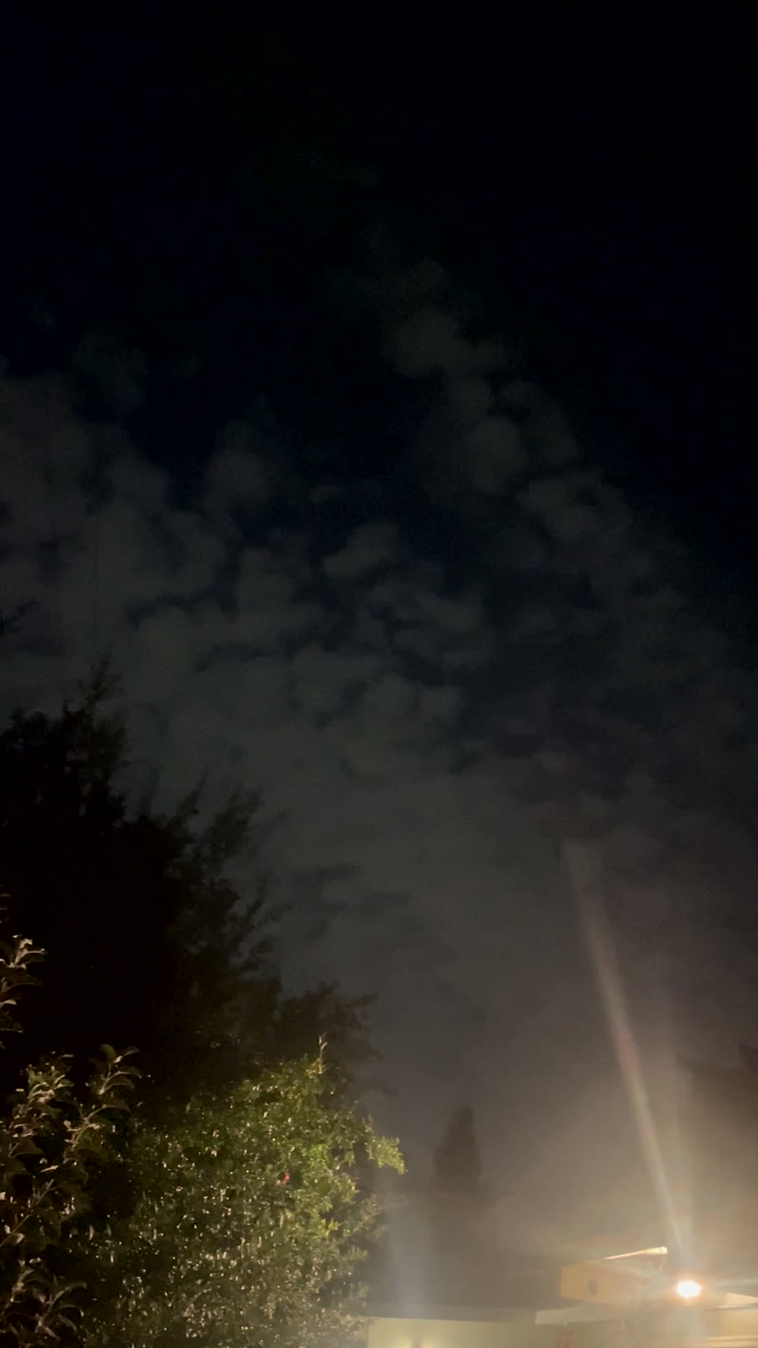 A bright lamp at a neighbouring roofline in the witness's second clip, throwing a long straight shaft of glare across the sky. Frame extracted by this archive from the original file. It demonstrates inside the witness's own footage that this camera produces prominent flare from a bright point source.