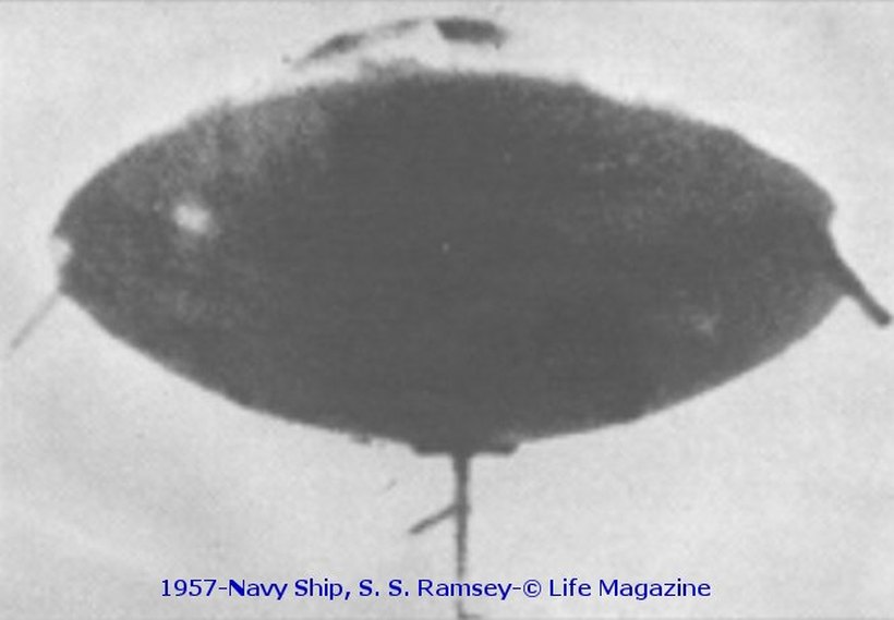 The canonical 1957 photograph attributed to radio officer Z. Thad Fogl aboard the SS Ramsay: a dark, lens-shaped disc with a thin vertical line trailing beneath it. The line is consistent with the silk thread later said to have suspended a model built from two F-104 Starfighter kit bases. The print carries a later, inaccurate caption naming a "Navy ship" and misspelling "Ramsey".