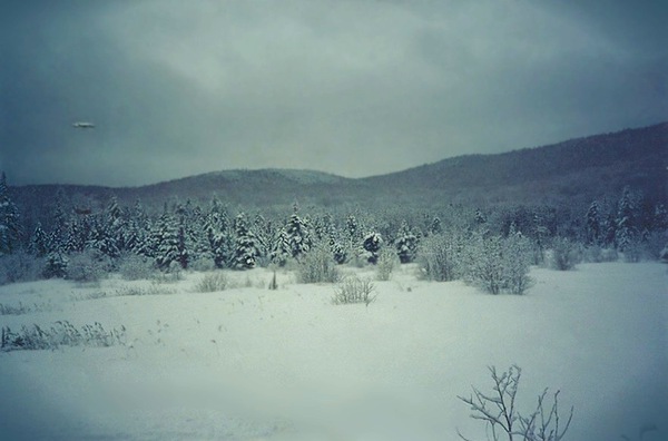 The single original photograph at the center of the case: a winter landscape at Stinson Lake, Rumney, New Hampshire, said to have been taken in the late afternoon of a February 2000 day. A small, faint, pale smudge sits high in the upper-left sky over the treeline; that smudge is the entire claimed "Mirror ship." This is the actual low-resolution photo as published, not a recreation, model or render.