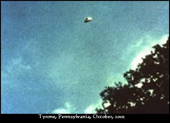 The image UFO Casebook attaches to this case, captioned "Tyrone, Pennsylvania, October, 2002," showing a small bright disc in a bright blue daytime sky above a tree line. This is almost certainly a miscaptioned stand-in, not the witness's real photograph. The witness's own account describes a roughly 7:30 PM, near-dark sky in which he "couldn't see any craft or object per se, just the bright light itself and the beam," with no visible structured craft, so a daylight saucer with no beam contradicts the testimony. The two actual Olympus photographs were never published by Stan Gordon or NUFORC.
